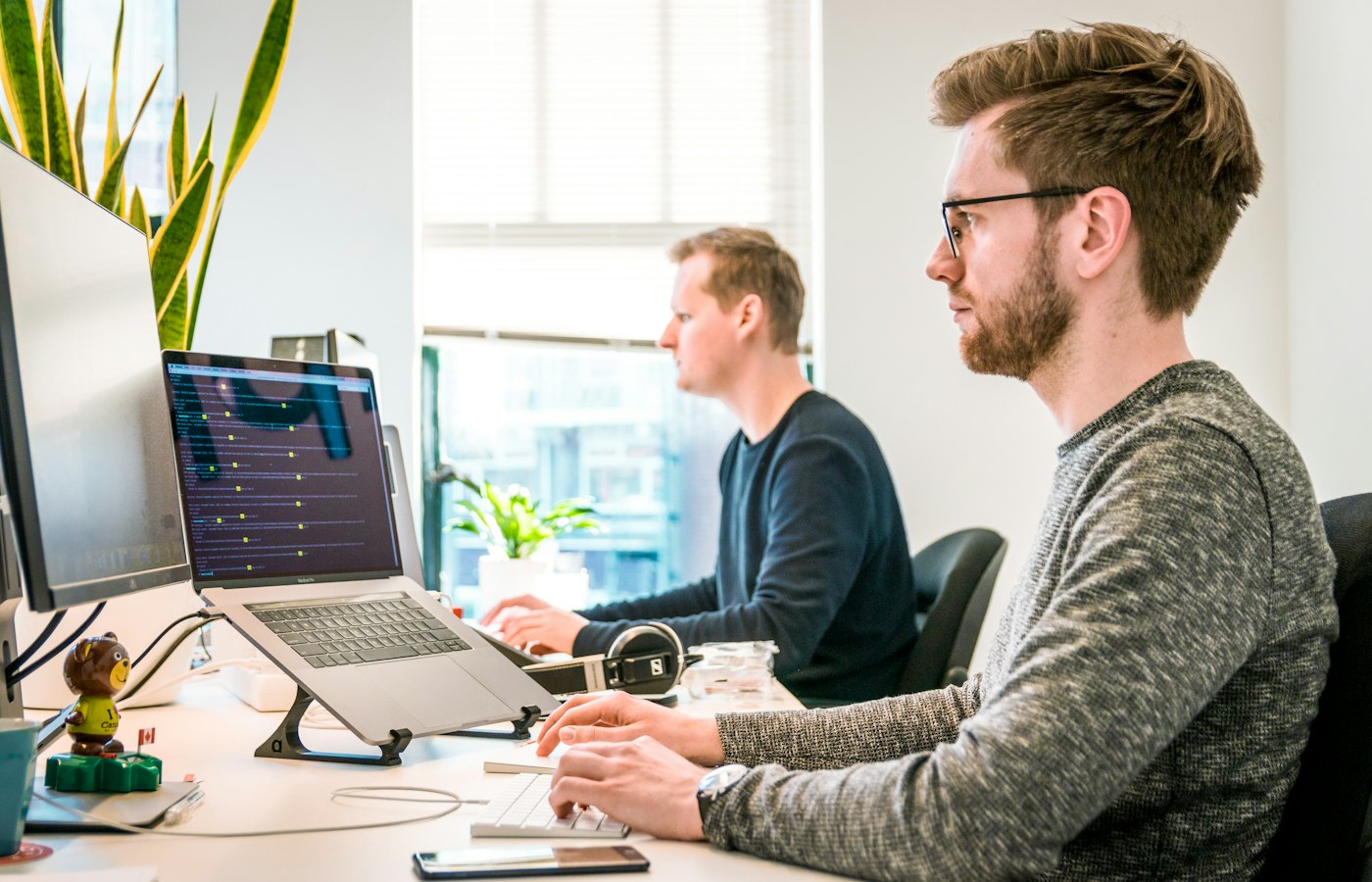 Dwóch programistów pracuje przy laptopach w jasnym biurze.